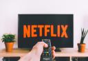 A person pointing a remote to a Netflix logo on a TV. Credit: Canva