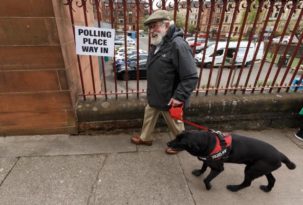 Glasgow Times: Pictured is a man with his dog arriving to vote at the polling place at Notre Dame primary school in Glasgow to cast his vote in the council elections