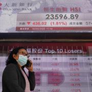 A woman wearing face mask walks past a bank electronic board showing the Hong Kong share index at Hong Kong Stock Exchange Monday, March 16, 2020. Asian stock markets and U.S. futures fell Monday after the Federal Reserve slashed its key interest rate to