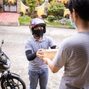 A delivery person drops off a parcel to a man with both people wearing facemasks. Credit: Canva