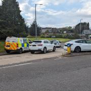 A car passes along the reopened road between the police vehicle and a white vehicle stranded on a traffic island following the incident