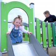 The play area has a castle-themed climbing unit, a toddler climbing unit, an accessible roundabout and trampoline, a range of swings including a basket swing, and a cable way