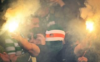 A Celtic fan wearing a balaclava sets off two flares at a match
